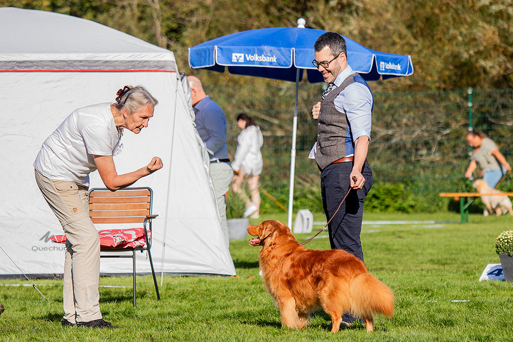 Edison steht lächelnd frontal vor der Richterin, die eine Faust ballt, um seine Aufmerksamkeit zu bekommen