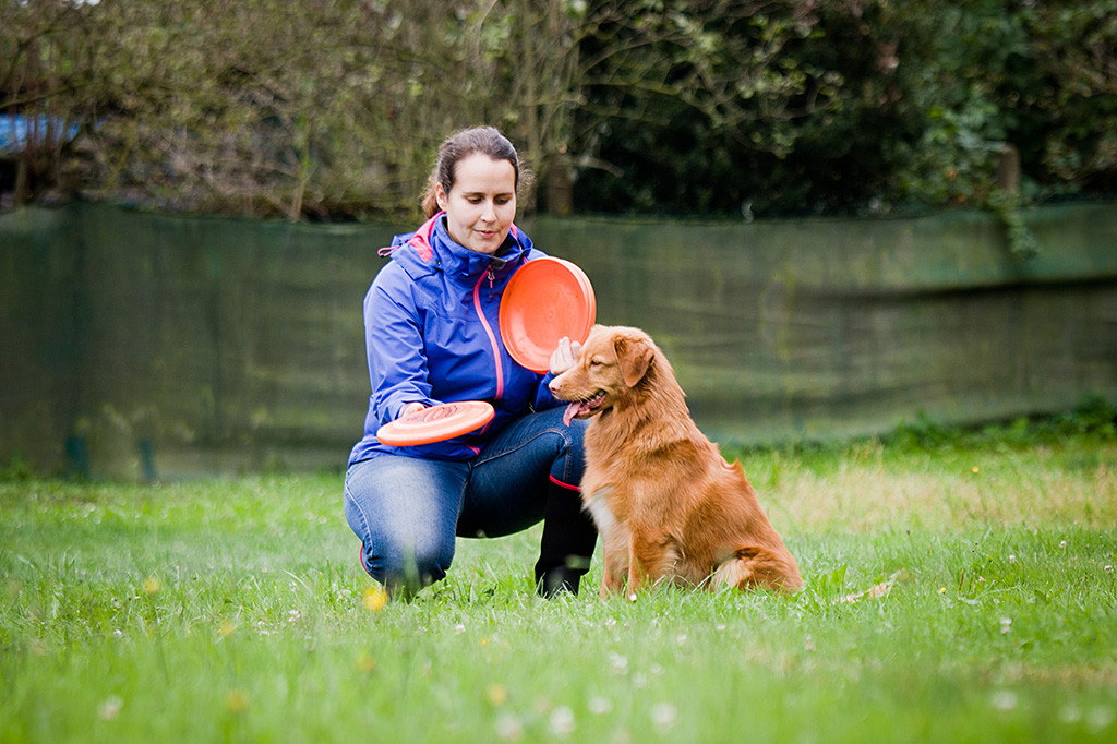 Ivalu bekommt von eine hockenden Carina Frisbees gezeigt