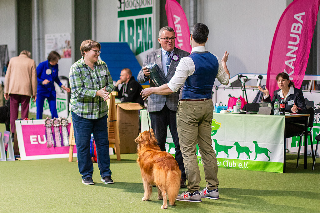 Edison steht zusammen mit der Ringhelferin, dem Richter und Stephan im Ring, die sich lachend während der Preisübergabe unterhalten