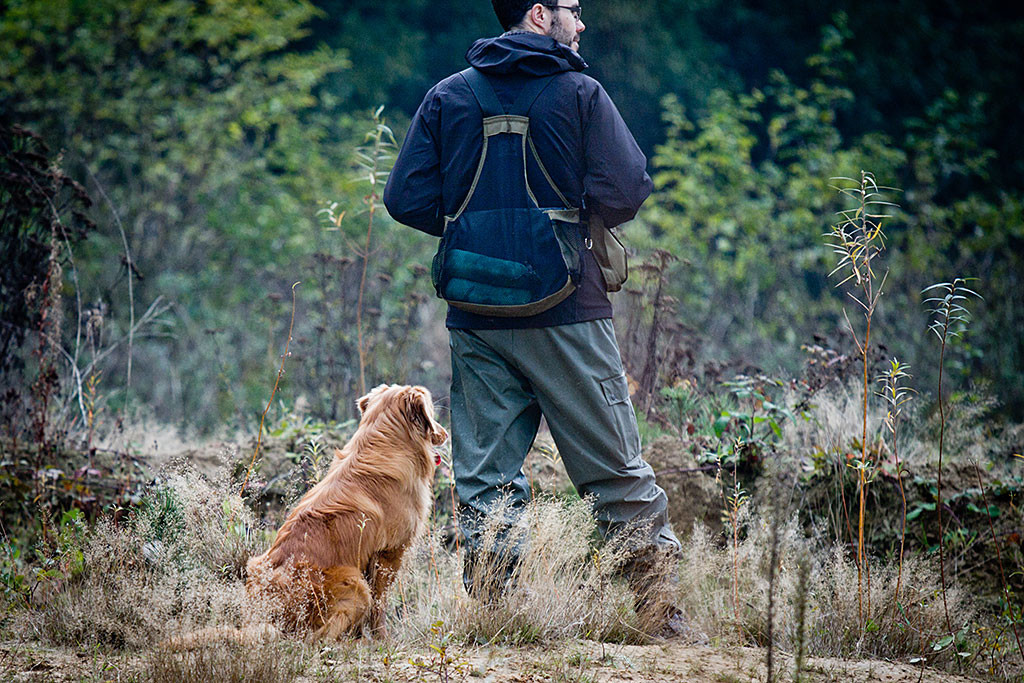 Edison sitzt neben Stephan, die beide entspannt dem anderen Hund bei der Suche zuschauen