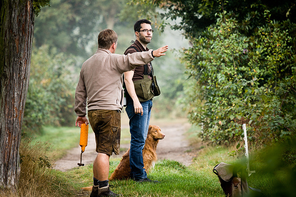 Edison sitzt neben Stephan und schaut auf den See raus, Carsten erklärt gestikulierend die nächste Aufgabe