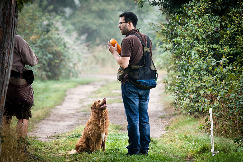Edison steht vor Stephan, der einen Wasserdummy in der Hand hält, und schaut zu ihm hoch, neben ihnen steht Carsten