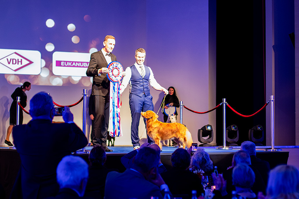 Newton steht mit Stephan auf der Bühne, der Richter steht daneben und hält die große Schleife in die Höhe, im Publikum werden Fotos gemacht