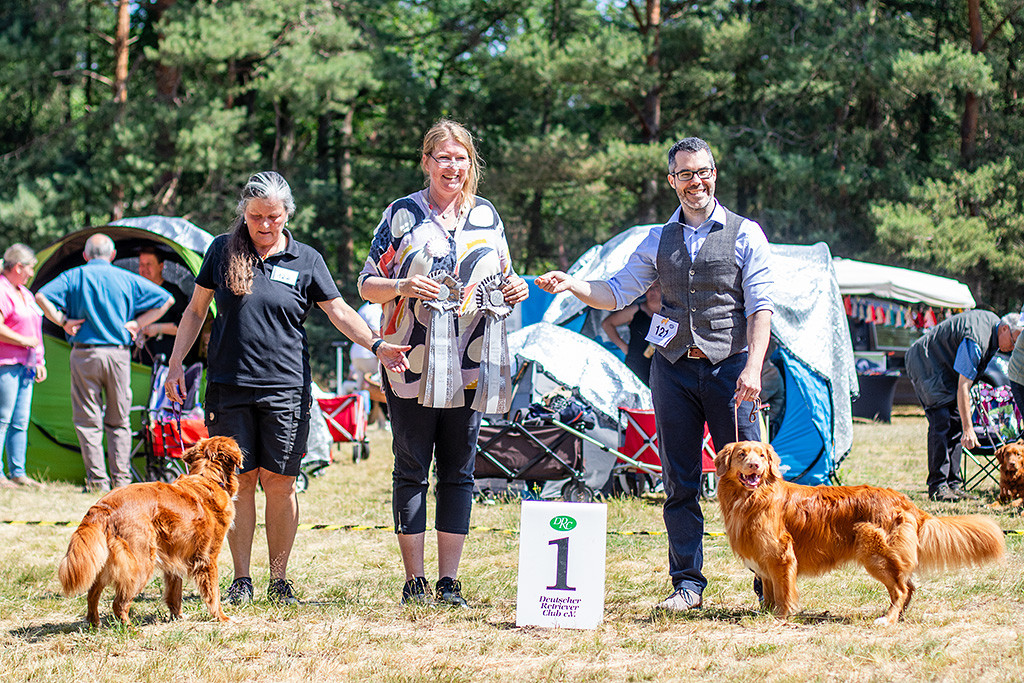 Newton posiert mit der Hündin fürs Siegerfoto, dahinter stehen ihre Besitzerin, die Richterin und Stephan