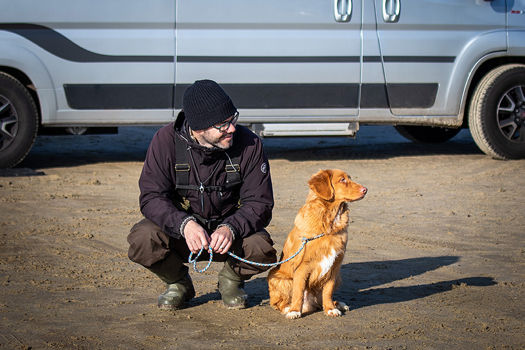 Newton sitzt angeleint neben Stephan, der sich gerade hingehockt hat