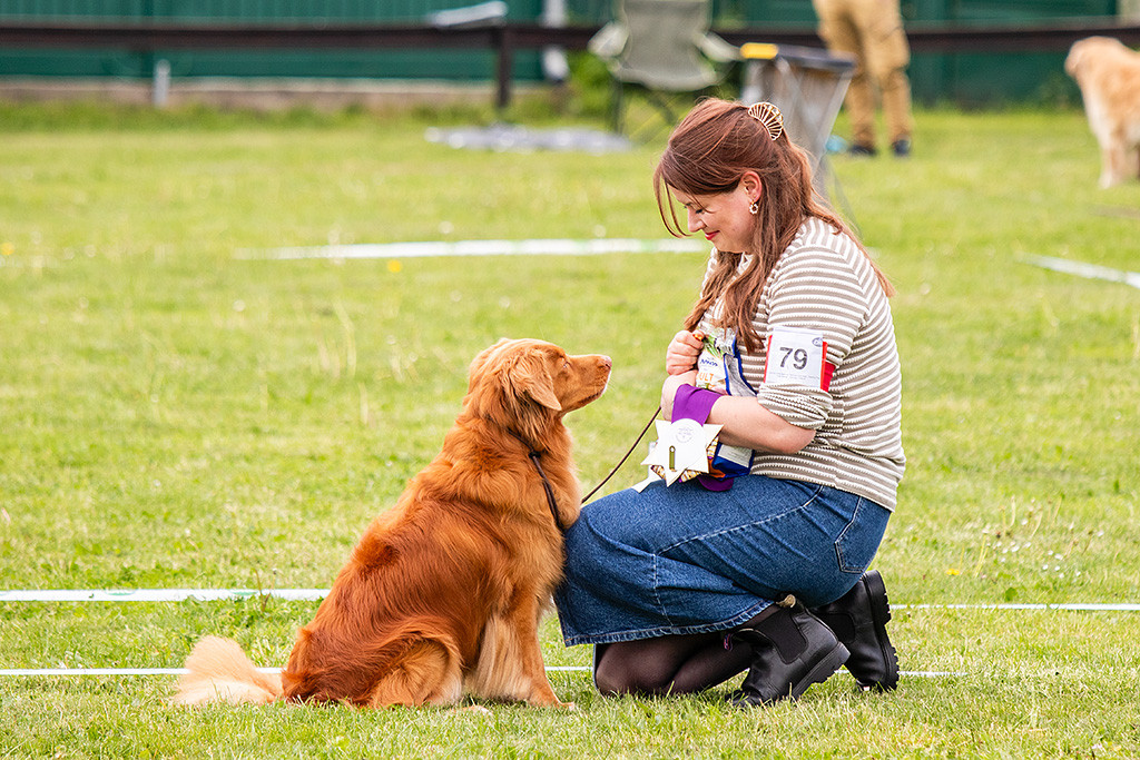 Edison sitzt vor Ann-Kathrin, die lächelnd die Best Veteran Schleife in der Hand hält und schaut zu ihr hoch