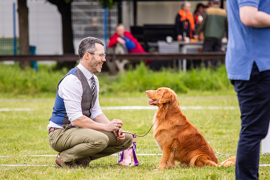 Newton sitzt frontal vor Stephan, der vor ihm hockt, beide lächeln sich an
