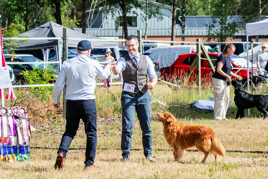 Edison lächelt den Richter an während er Stephan zum Gewinn des Rassebesten gratuliert und ihm die BOB-Schleife übergibt